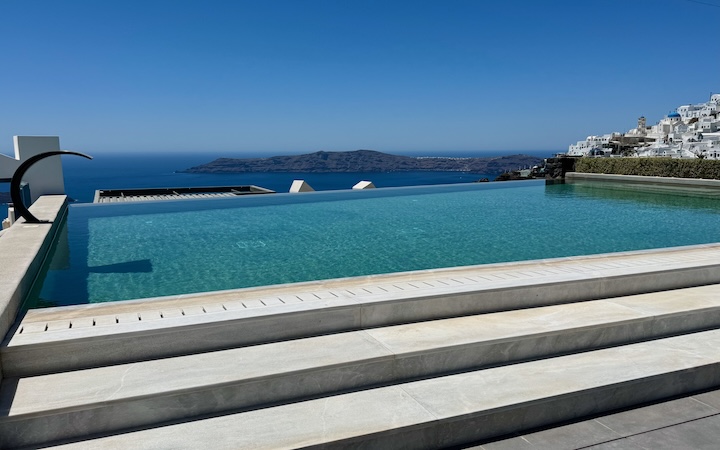 Three steps lead up to an infinity pool overlooking the caldera with the Imerovigli village and Thirassia Island in the background at Aeifos Boutique Hotel in Imerovigli, Santorini.