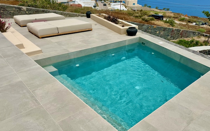 View down into a private pool on a terrace next to two double-sized sunbeds on a hill above the sea at Ethos Vegan Retreat in Imerovigli, Santorini.