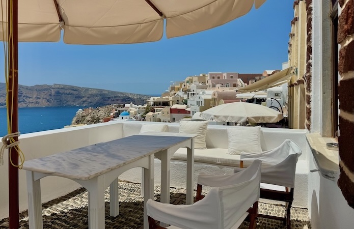 A marble table shaded by an umbrella on a private terrace overlooking the caldera at 1864 The Sea Captain's House in Oia.