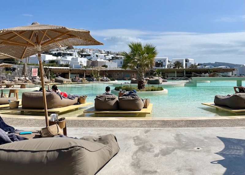 A lagoon-like pool with small islands of trees and sunbeds with more sunbeds around the edge at Andronis Arcadia in Oia, Santorini.