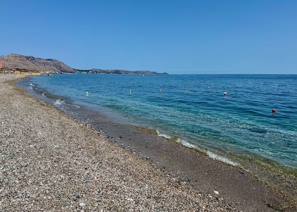 A sand-and-pebble beach with calm, clear water stretching into the distance at Kiotari, Rhodes.