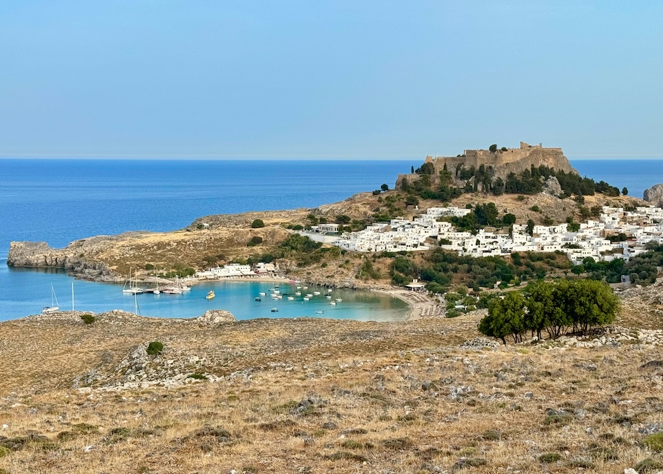 The city of Lindos, made of square white buildings, spreads out below the Acropolis and sits just above the beach in a crescent-shaped bay in Rhodes.