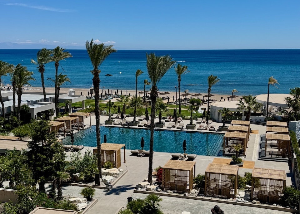 View from above a pool ringed with cabanas and sunbeds and facing the beach at Ammades resort in Faliraki, Rhodes.