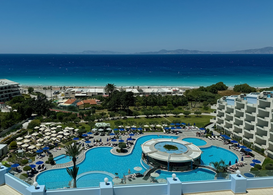 View overlooking the Atrium Platinum Resort centered around an enormous, freeform pool, surrounded by green lawn and facing the sea in Kritika, Rhodes.