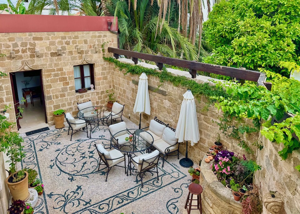 A garden courtyard with a pebble mosaic floor, stone walls, and a pair of al fresco dining tables at Hotel Ellique in Rhodes Old Town.