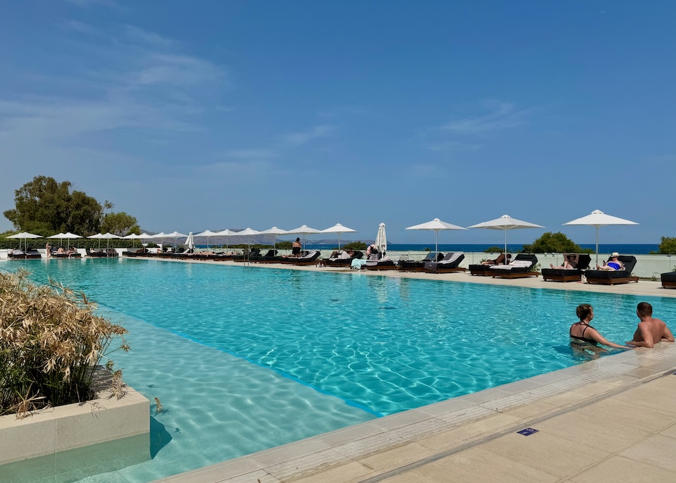 A long pool lined with sunbeds and umbrellas with the sea in the distance at Gennadi Grand resort in Rhodes.