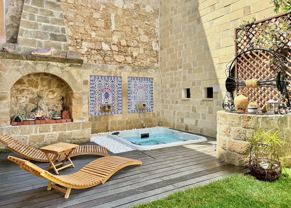 A modern deck with a sunken jacuzzi and sunbeds set in a medieval courtyard with an old well and outdoor fireplace at In Camera Art Hotel in Rhodes Old Town.