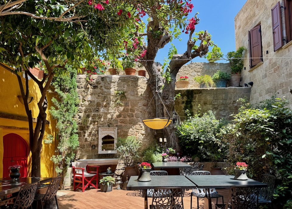 A colorful garden courtyard in a medieval building set with dining tables at Kokkini Porta Rossa in Rhodes Old Town.