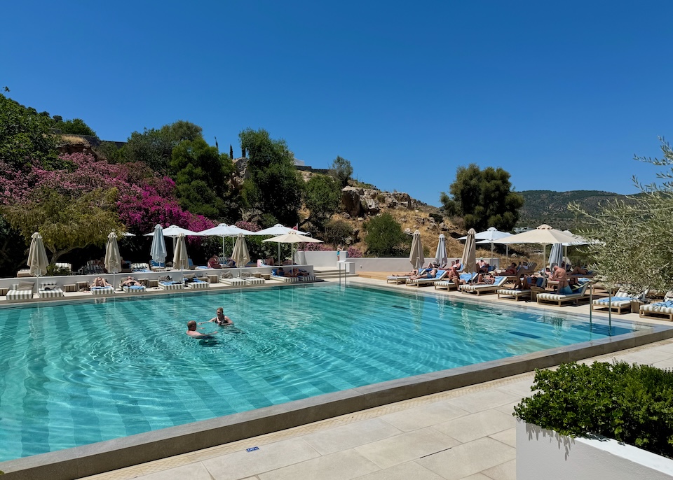 A swimming pool with sunbeds and umbrellas lining two sides at Lindos Mare resort in Rhodes.