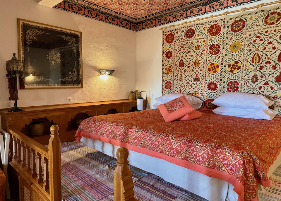 A vibrant mix of Ottoman-inspired textiles on the bed, walls, and floors with a mosaic ceiling and antique helmet at Melenos Art Hotel in Lindos, Rhodes.