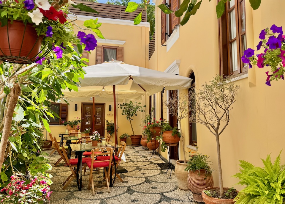 A garden courtyard filled with colorful flowers and trees in clay pots, a pebble mosaic floor, and three picnic tables at Rodos Niohori hotel in Rhodes.