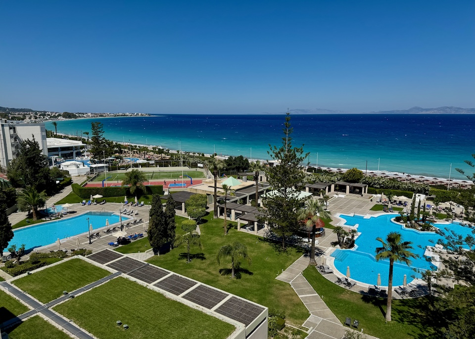 Two freeform pools and two sports courts set in a green lawn facing the beach and sea at the Sheraton Rhodes Resort in Ixia.