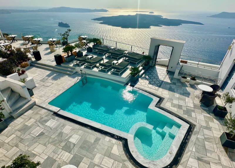 View over the sun terrace of a hotel on the Santorini caldera, with a free-form pool and hot tub.