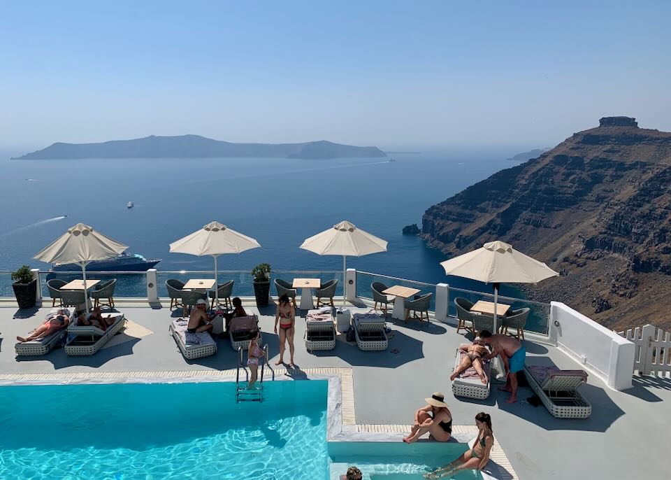 Guests enjoying a hotel swimming pool overlooking the Santorini caldera in Firostefani