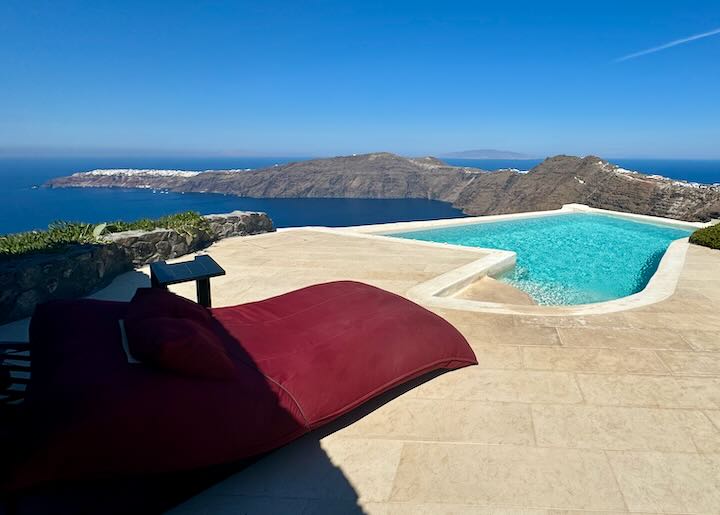 Red sun bed next to an infinity pool overlooking the Santorini caldera.