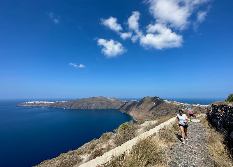 Two people walk along a stone path skirting the Santorini Caldera.