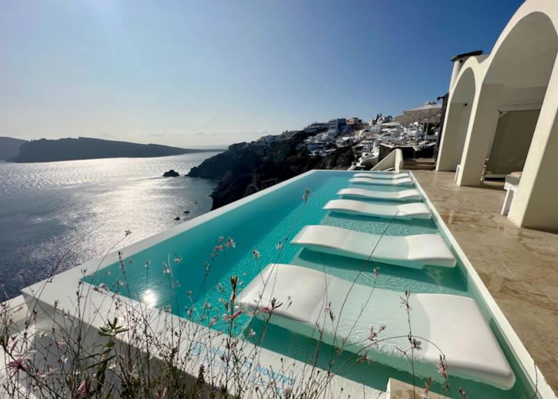 Sparkling hotel infinity pool with floating sun beds, overlooking the Santorini caldera.