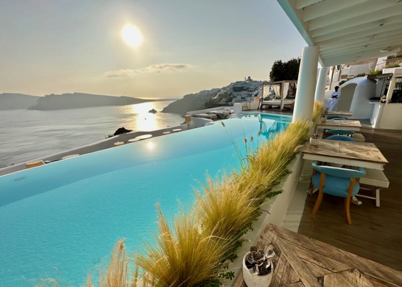 Cafe tables and mediterranean grasses next to a sparkling blue sea-view infinity pool.