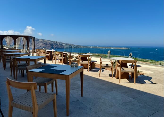 Tables set on a hotel pool terrace with view of the Aegean Sea