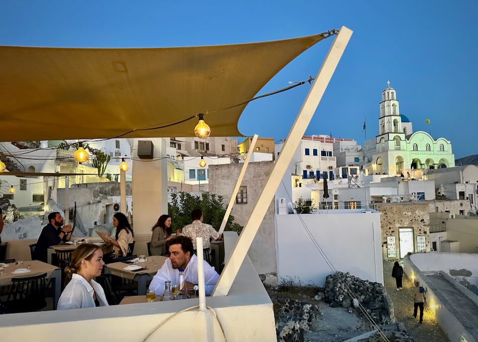 People dine at a rooftop terrace in a rustic Greek village.