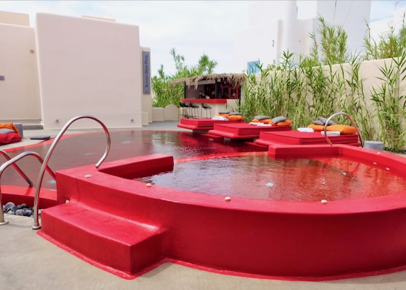 Red hotel swimming pool with red sun loungers and a pool bar with red stools.