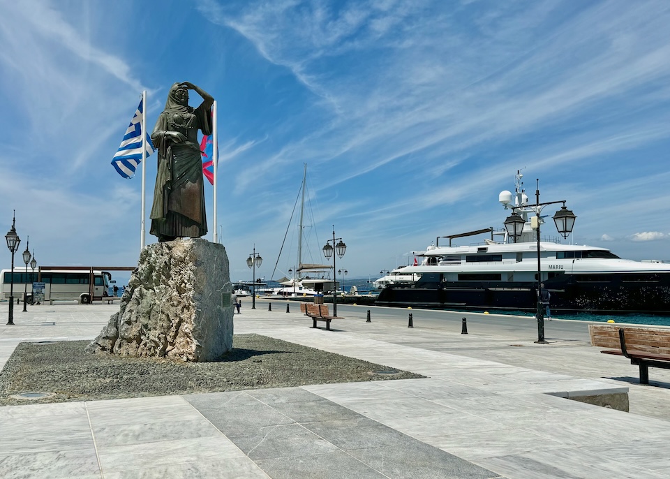 Statue of a woman shielding her eyes from the sun with her hand in the port with boats in the background in Dapia, Spetses.