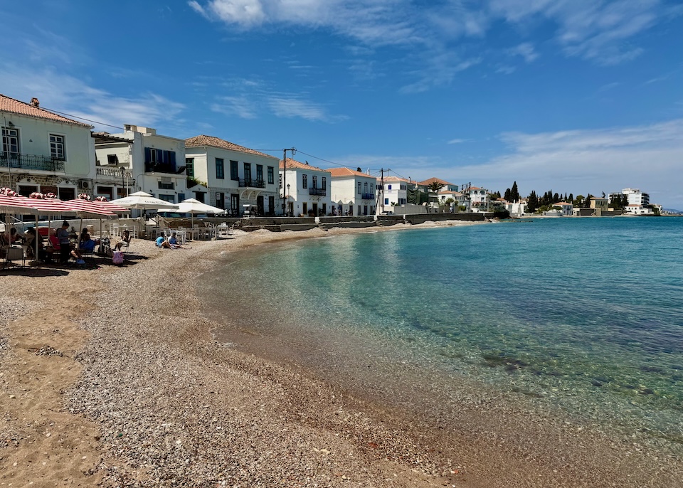 A half-moon shaped bay with a sand-and-pebble beach set with umbrellas and sunbeds in Kounoupitsa, Spetses.