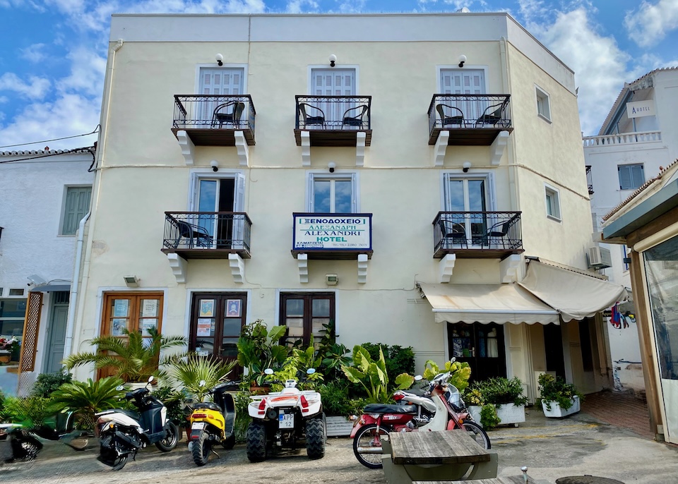 Exterior of Alexandris Hotel with a palm garden in front and scooters and ATVs parked in Spetses.