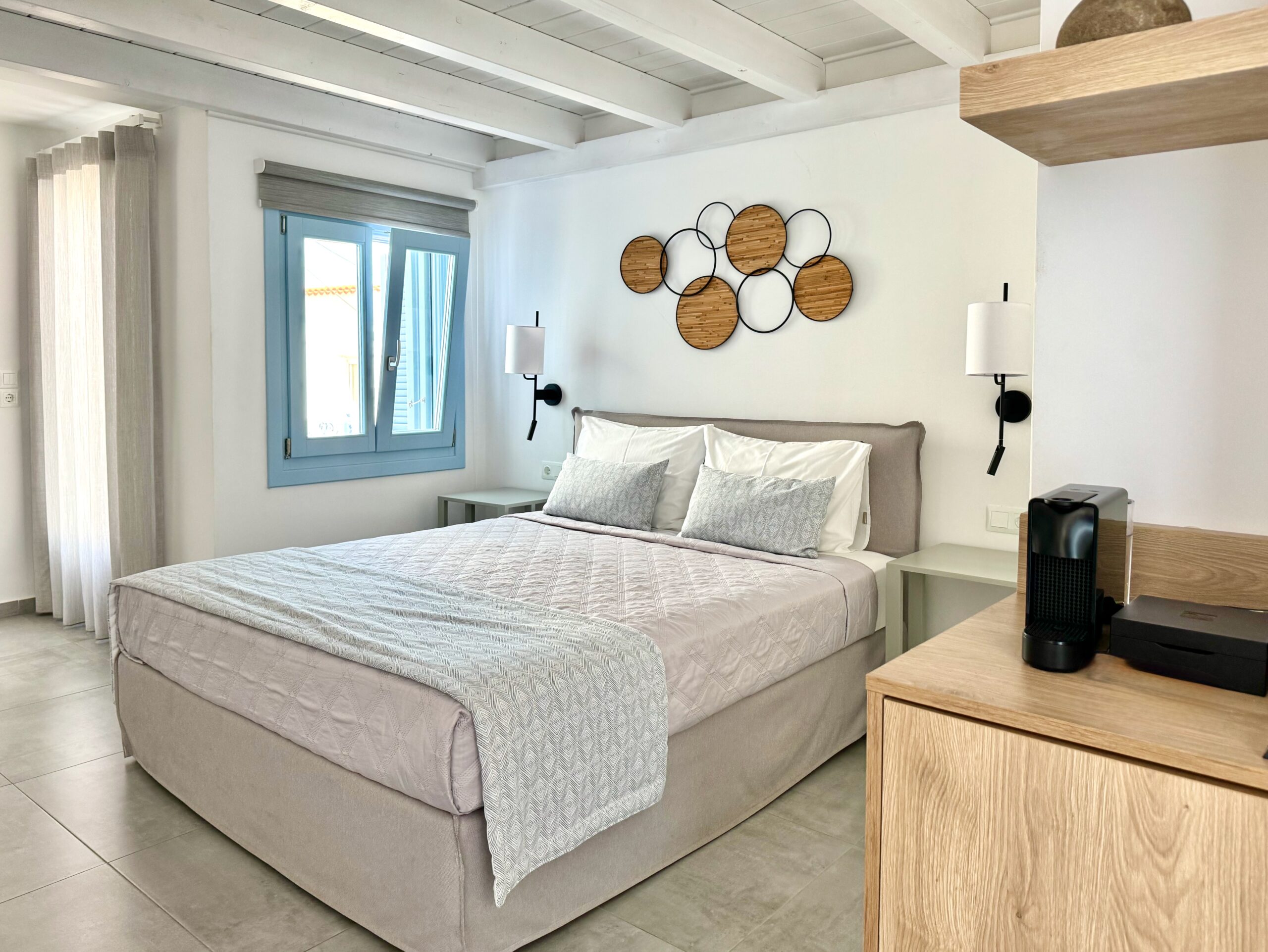 A sunny guest room with exposed beams in the ceiling and a queen-sized bed at Lumiere hotel in Spetses.