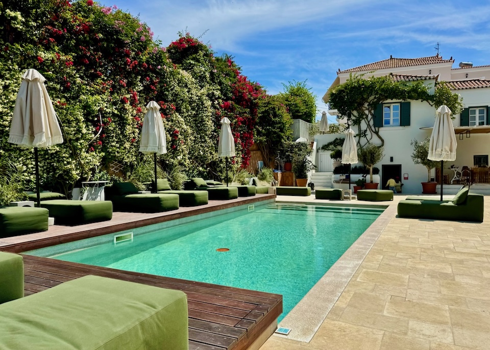 A pool lined with sunbed and umbrella sets in a garden courtyard at Yayaki Hotel in Spetses.