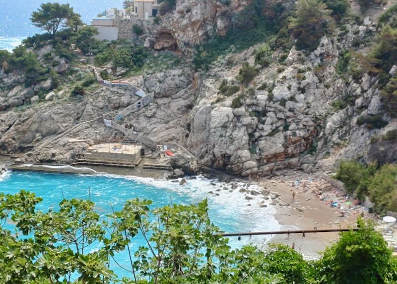 A view from high up looking down on a beach with clear blue ocean water.