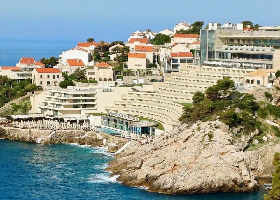 A hotel sits on terraces down a hill to a pool by the ocean.