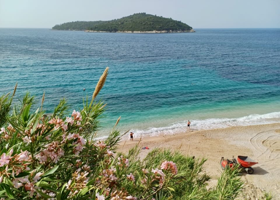 A view looking down at a tan sandy beach blue water and a green island in the distance.