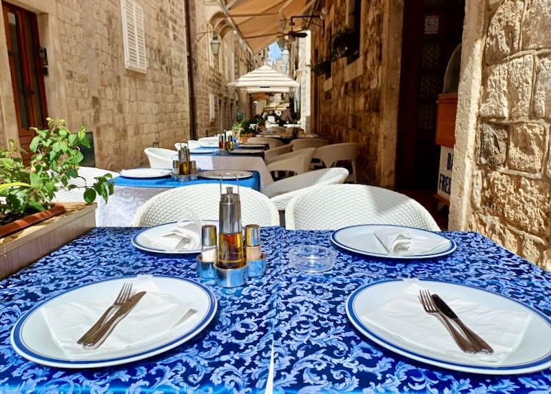 A bright blue table cloth covers a table outdoors along a stone passageway.