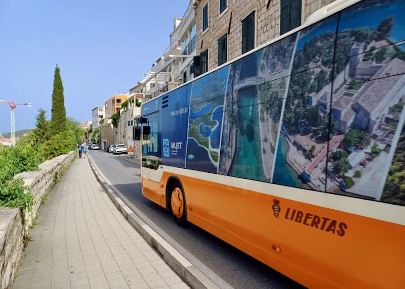 A bus rides down a single lane road next to a sidewalk.