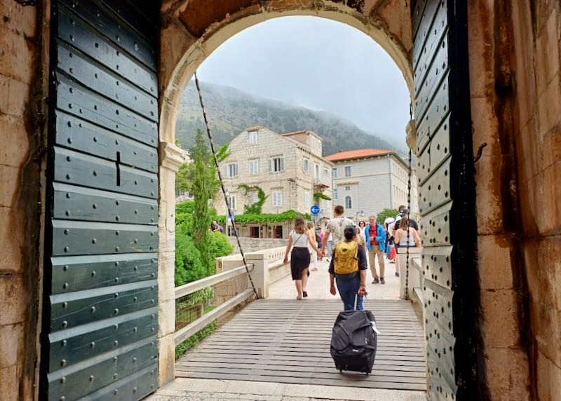 People walk through a large rounded entrance to a walled city.