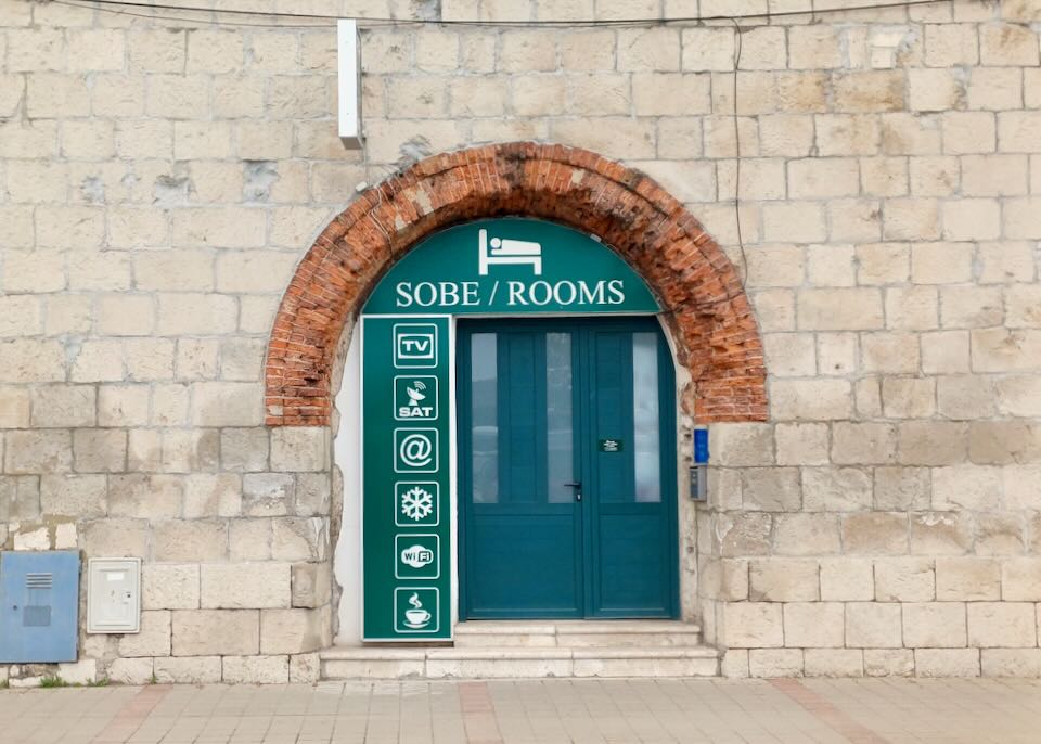 A tan stone wall has an rust brick-colored arch and a green door.