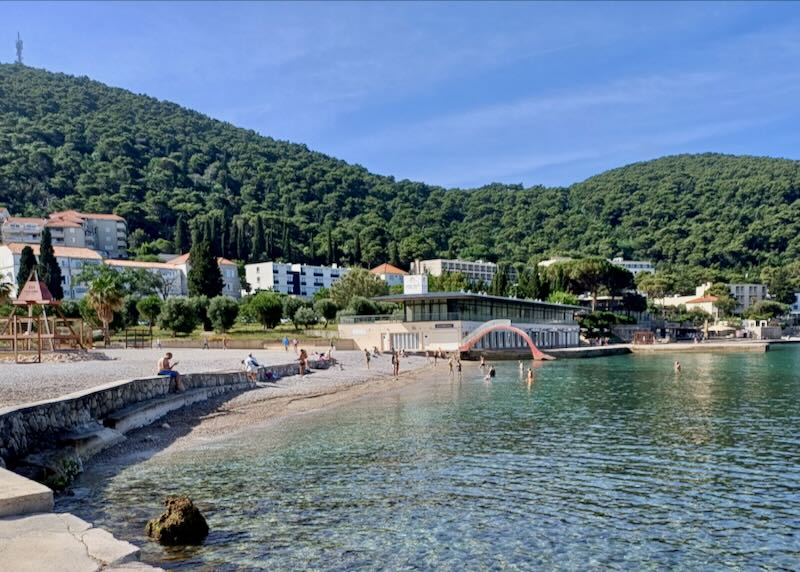 People swim in clear blue water on a rocky beach.