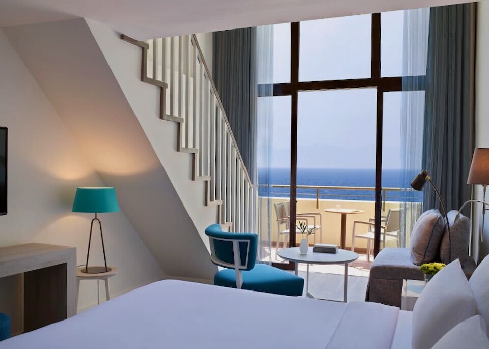 A split-level, sea-view room with a bed in the foreground and steps leading up to the loft at Amus Hotel in Rhodes.