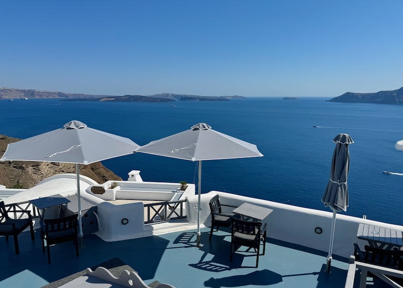 A caldera-view terrace with two-seater tables at Aspa Villas in Oia.