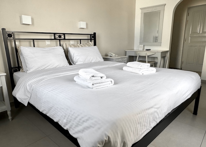 A clean, white, simple bedroom at Pelican Hotel in Fira.