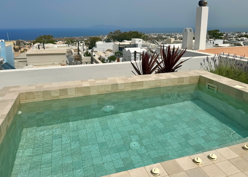 A rooftop jacuzzi with views over Fira village toward the sea at Ethos Vegan Suites in Santorini.