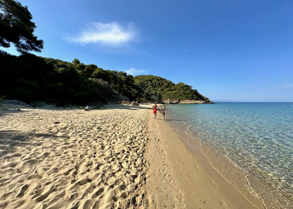 A couple walks along a wide golden sand beach on a sunny day