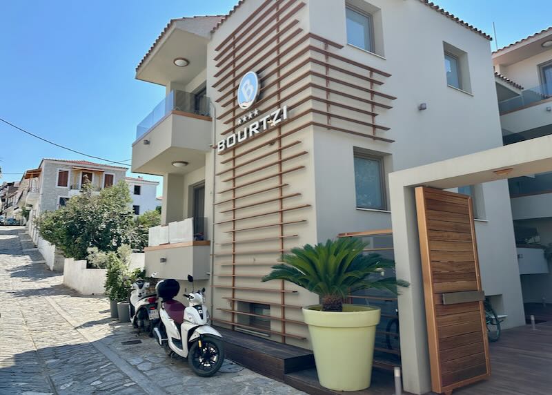 Exterior of a boutique hotel on a narrow Greek lane, with a motorscooter parked in front.