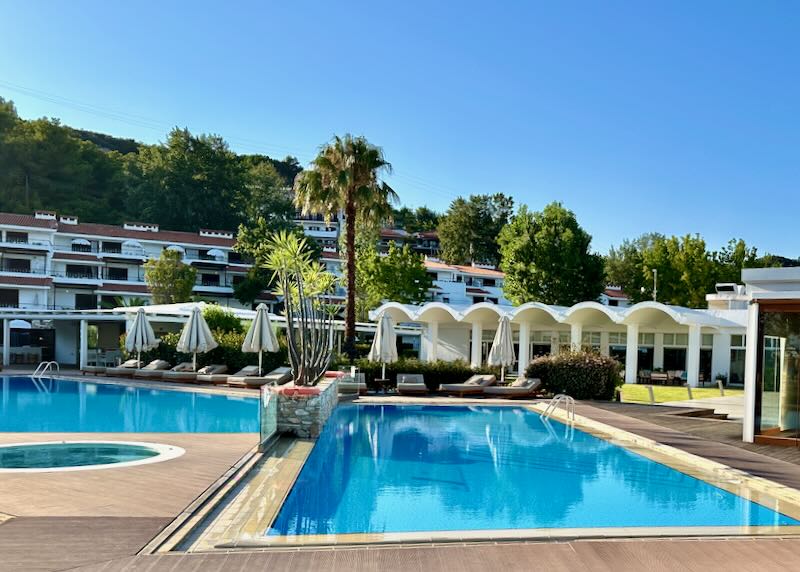 Hotel swimming pool, with a white hotel and sun beds behind.