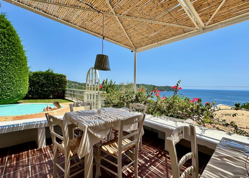 A woman lounges in a plunge pool next to a covered dining terrace overlooking the sea