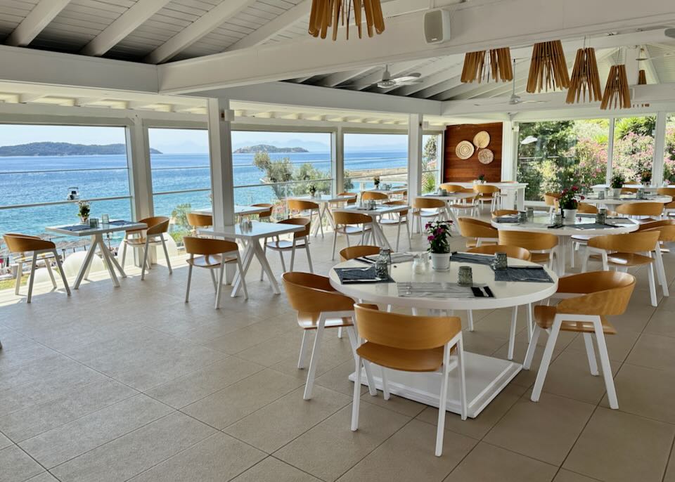 White tables set in a beachy open-air room overlooking the sea.