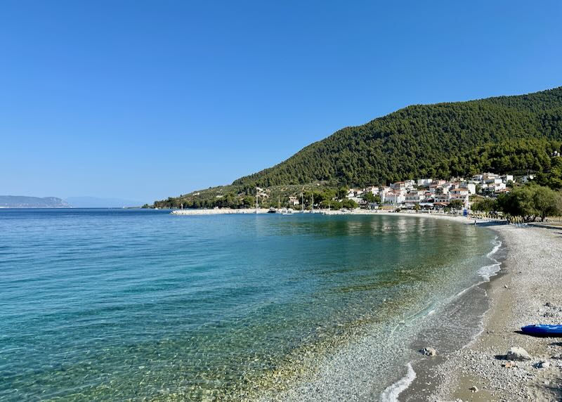 Emerald green water washes over a pebbly beach in Greece