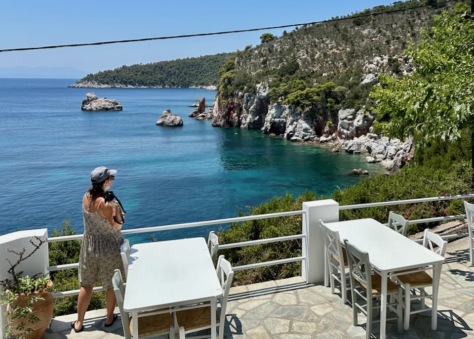 A woman points a camera at scenic rock formations over a beach.