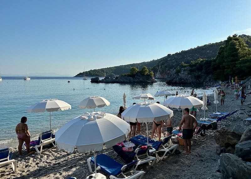 Late afternoon sun shines on sun umbrellas and sunbathers on a beach in Greece.